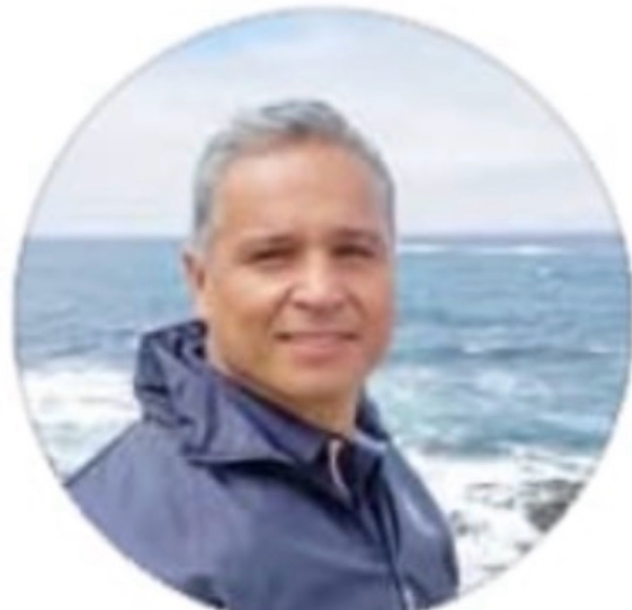 Circular portrait of a man wearing a jacket beside the sea.